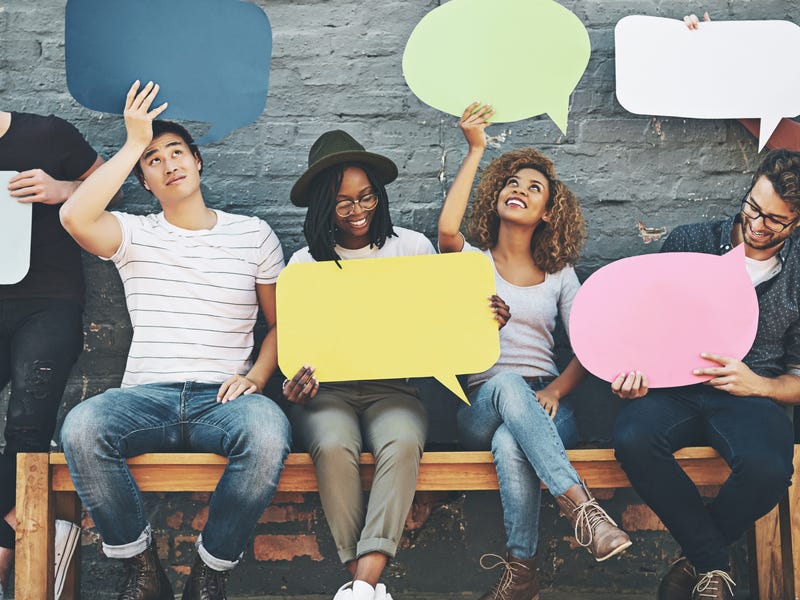 Mehrere Personen sitzen auf Bank und halten Papier in Sprechblasenform