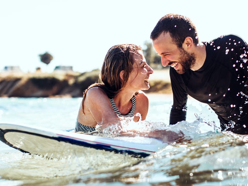 Ein junges Pärchen schwimmt mit einem Surfbrett im Meer.