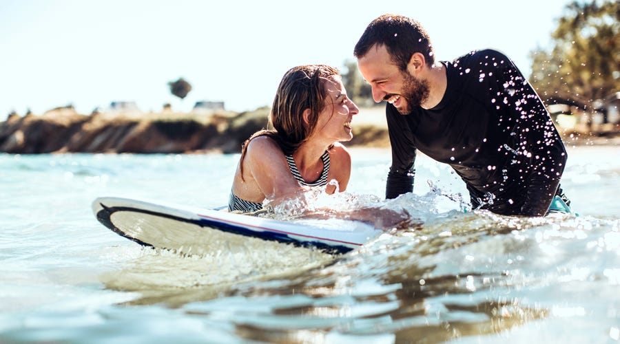 Ein junges Pärchen schwimmt mit einem Surfbrett im Meer.