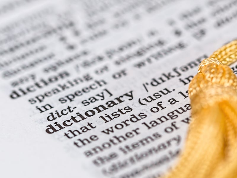 Aufgeschlagenes Wörterbuch mit Stoffquaste und sichtbarer Definition des Wortes "dictionary"