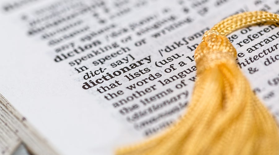 Aufgeschlagenes Wörterbuch mit Stoffquaste und sichtbarer Definition des Wortes "dictionary"