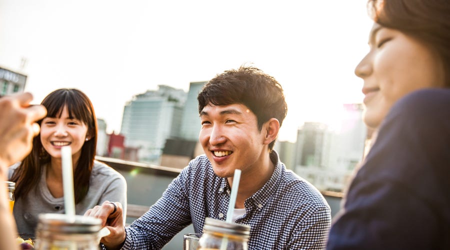 Junge Menschen sitzen an einem Tischen im Freien und lachen.