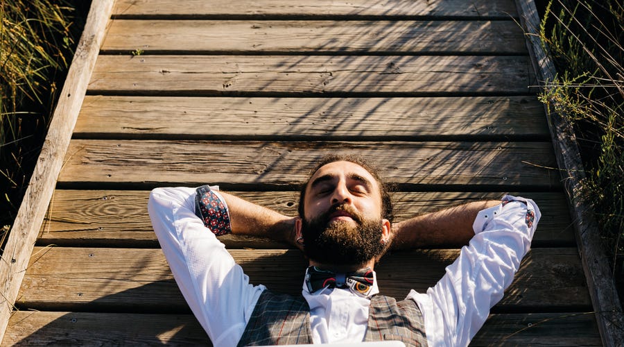 Ein Mann liegt mit verschränkten Armen auf einem Steg und träumt.