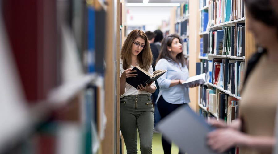 Frau liest in Bibliothek ein Buch.