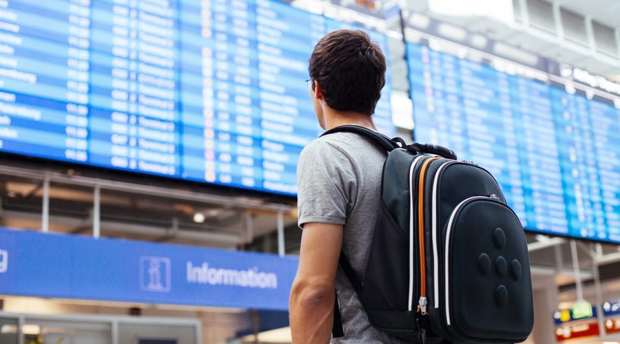 Mann steht am Flughafen vor Anzeigetafel.