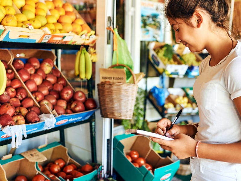 A young woman standing in front of a shelf with fruits.