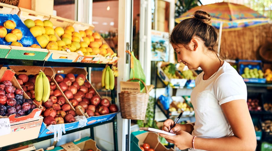 A young woman standing in front of a shelf with fruits.