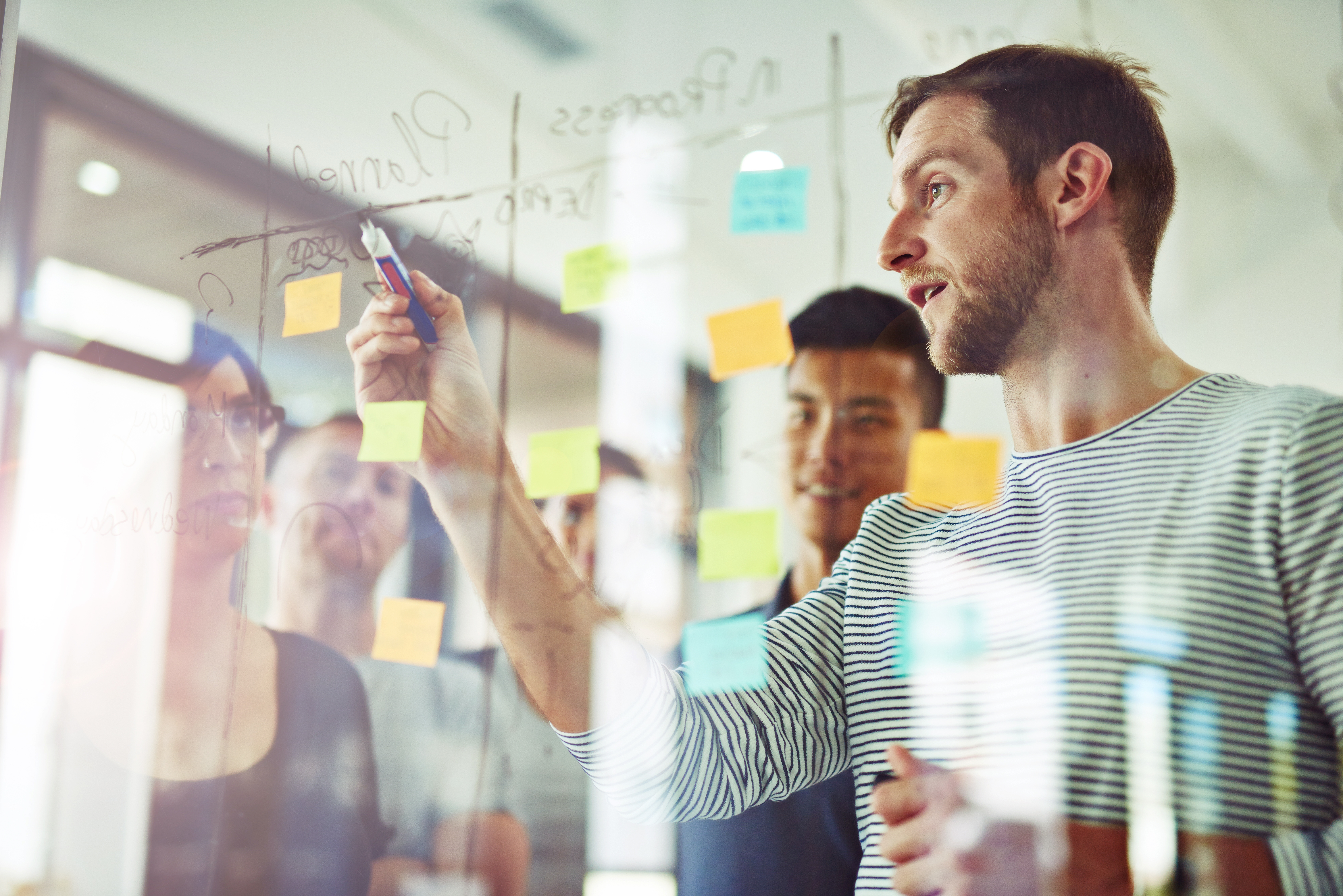 Mehrere Personen besprechen ein Projekt an einem Whiteboard.