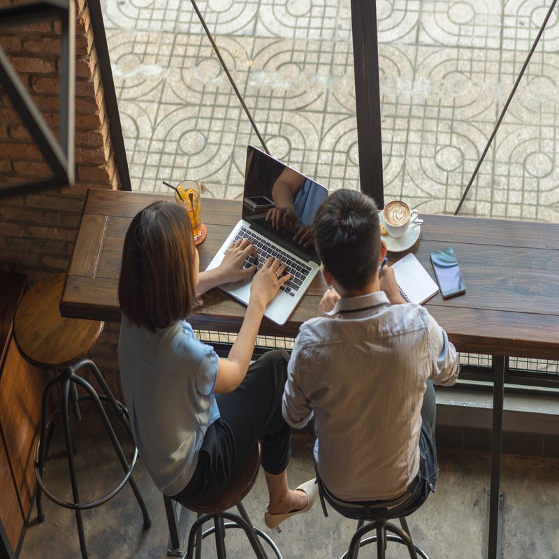 Zwei Personen sitzen vor einem Laptop und notieren sich etwas.