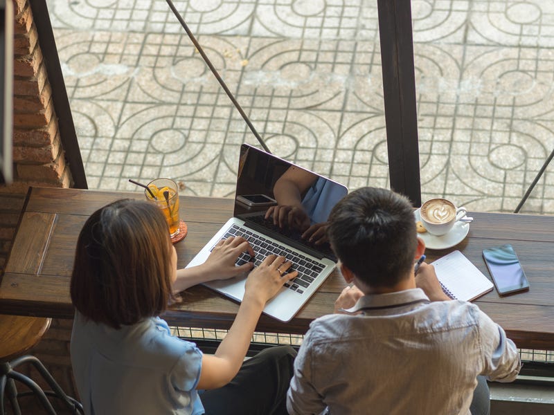 Zwei Personen sitzen vor einem Laptop und notieren sich etwas.