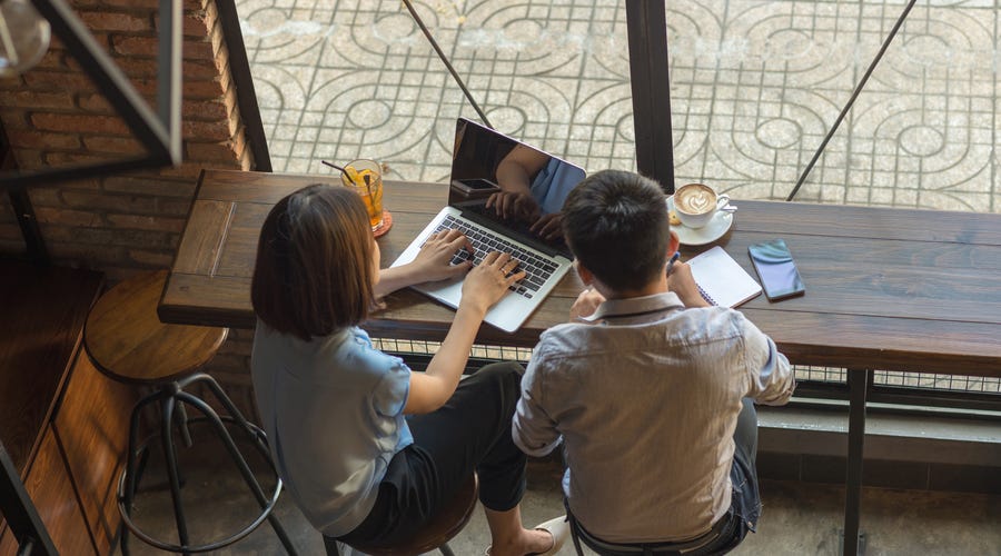 Zwei Personen sitzen vor einem Laptop und notieren sich etwas.