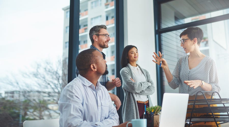 Mehrere Personen stehen in einem Büro um einen Tisch herum und besprechen etwas.
