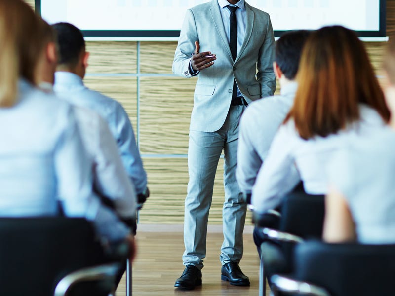 Mann hält Vortrag auf Englisch vor Menschenmenge.