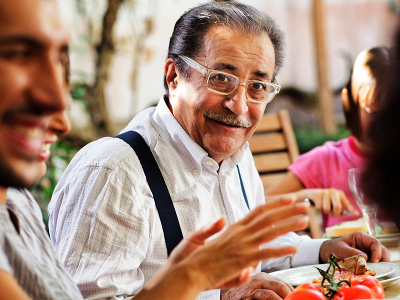 Älterer italienischer Mann sitzt mit Familie beim Essen am Tisch