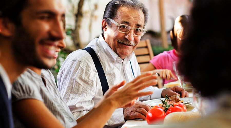 Älterer italienischer Mann sitzt mit Familie beim Essen am Tisch