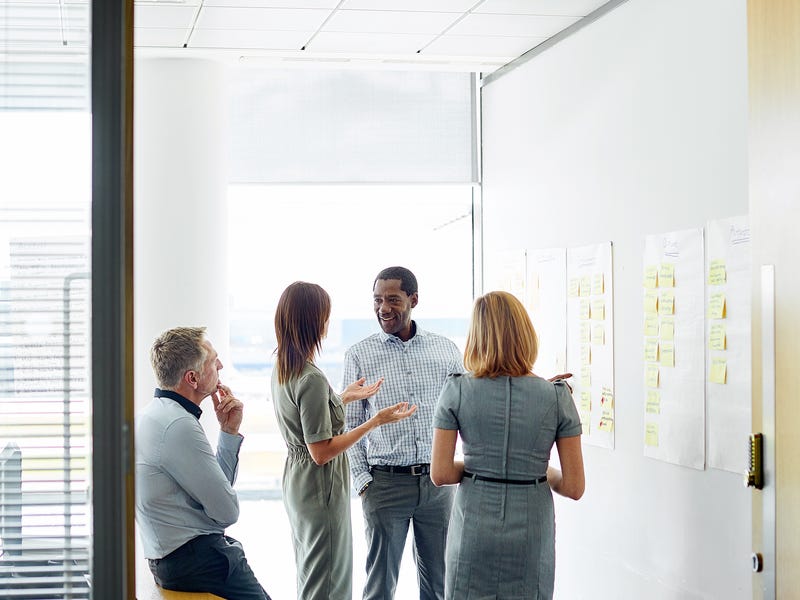 Vier Personen besprechen ein Projekt an einer Wand