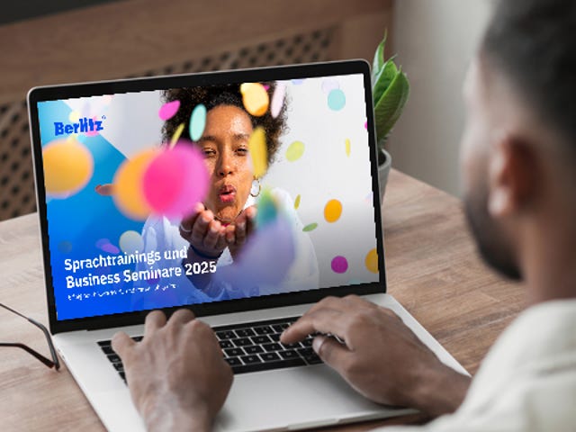 Ein Mann sitzt vor seinem Laptop und schaut sich den neuen Berlitz Katalog rund um Sprachtrainings und Business Seminare an.