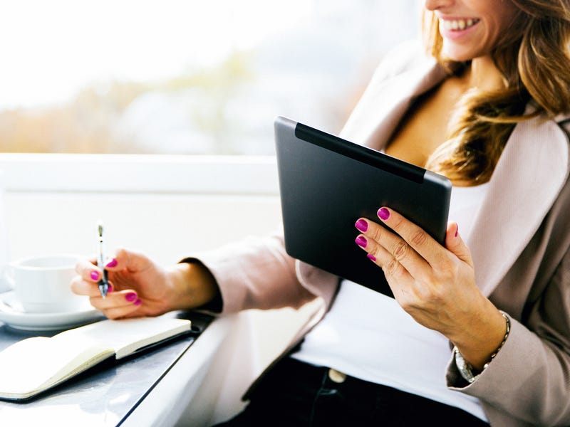 Eine Frau sitzt mit Tablet und Block am Tisch.