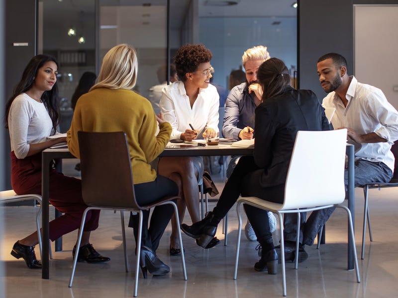Gruppe Menschen sitzt gemeinsam am Tisch und bespricht Arbeit.