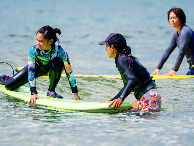 Kinder sitzen im Wasser auf einem Surfboard.