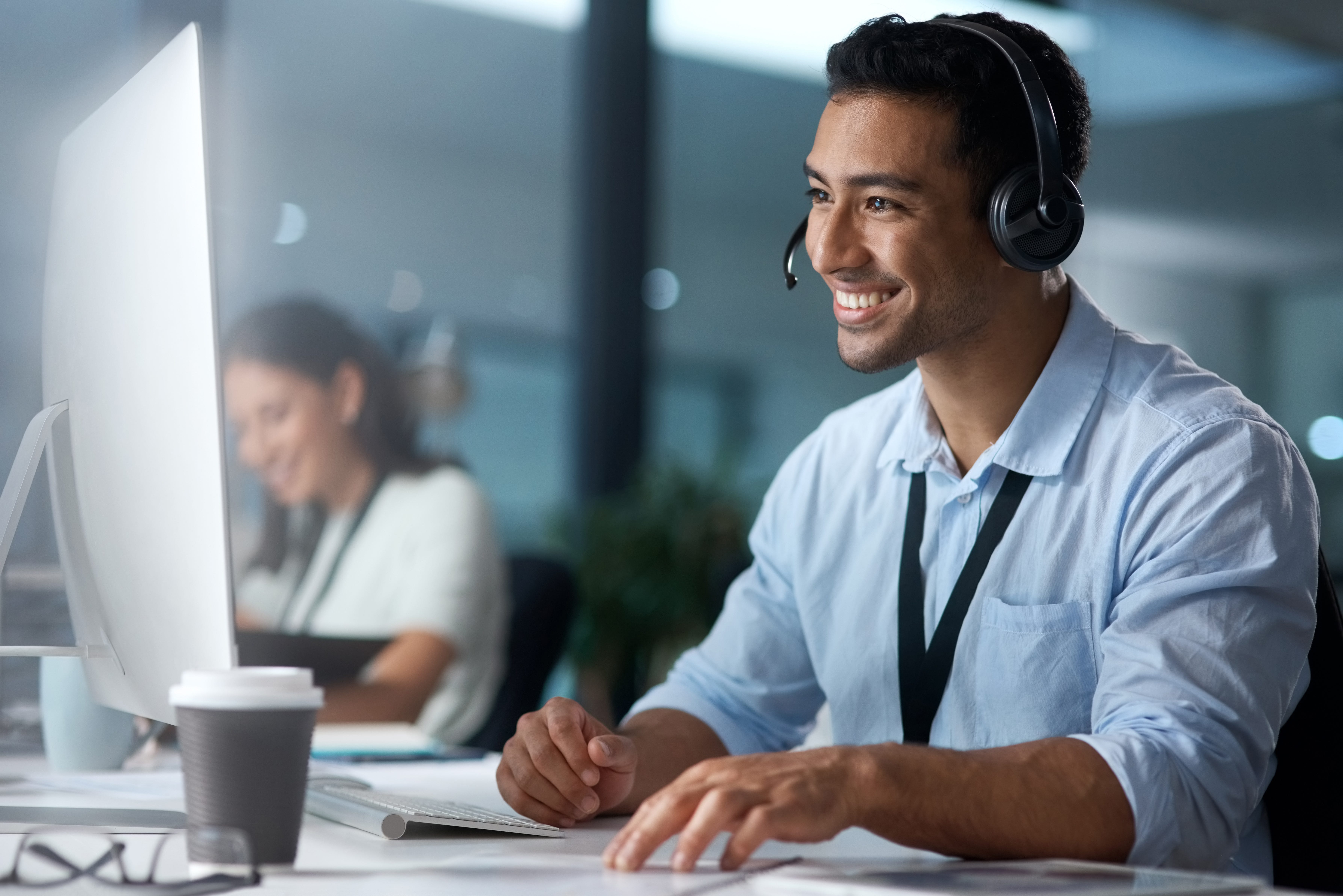 Mann sitzt mit einem Head-Set auf dem Kopf lächelnd vor einem Computer