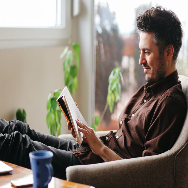 Ein Mann sitzt auf einem Sessel und liest ein Buch.