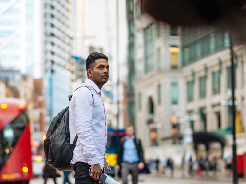 A man walking across a road in a large city.