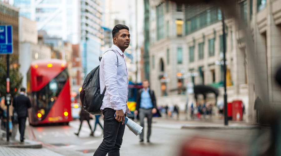 A man walking across a road in a large city.