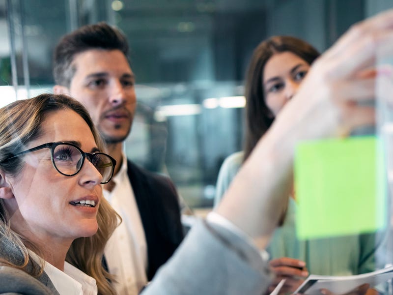 Drei Personen stehen an einer Tafel und besprechen etwas.
