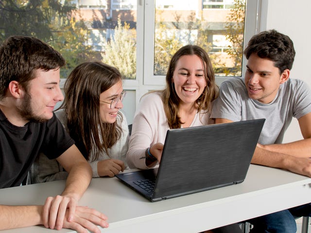 Drei Jugendliche sitzen mit ihrer Trainerin vor einem Laptop und besprechen eine Aufgabe aus dem Programmier- und Sprachkurs.