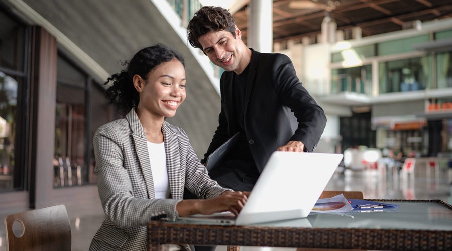 Ein Mann und eine Frau sitzen vor einem Laptop und der Mann zeigt lächelnd auf den Bildschirm.