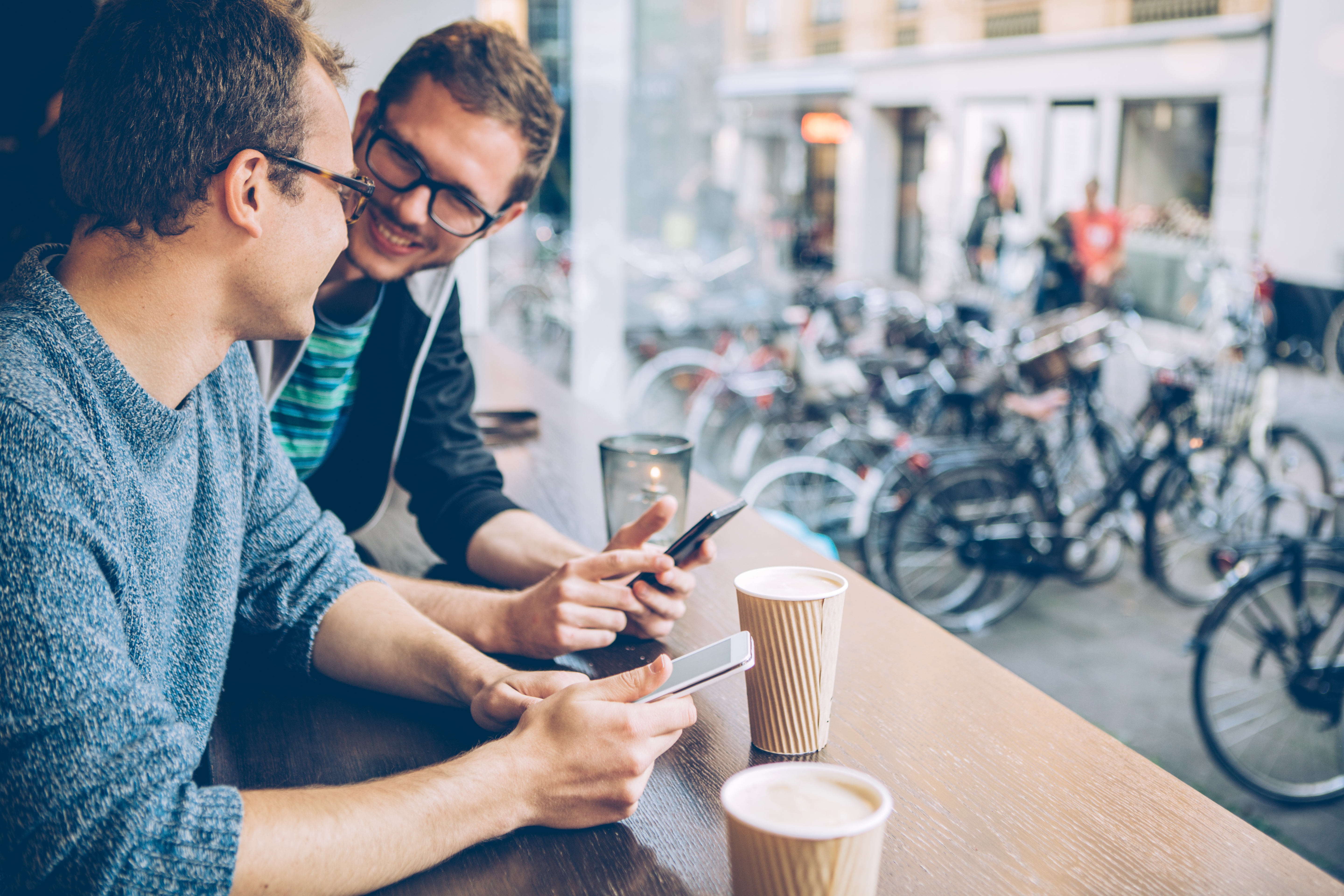 Zwei Männer sitzen mit Smartphones bei einem Kaffee zusammen