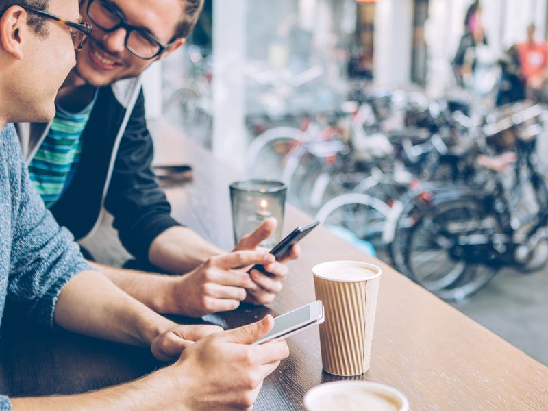Zwei Männer sitzen mit Smartphones bei einem Kaffee zusammen
