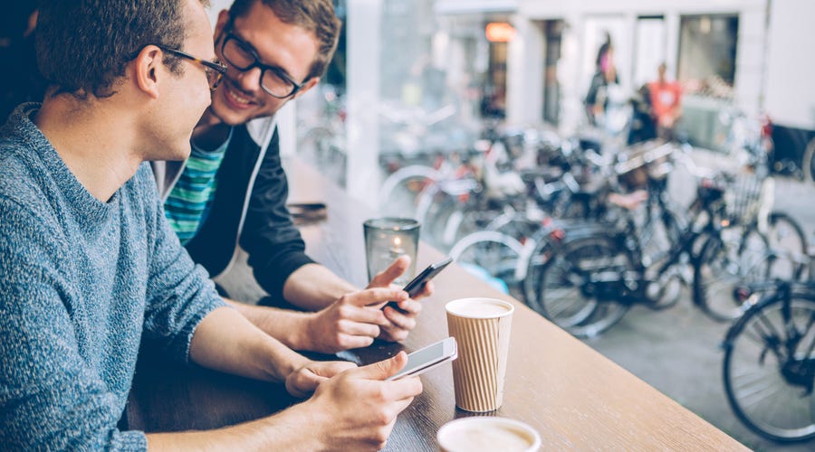 Zwei Männer sitzen mit Smartphones bei einem Kaffee zusammen