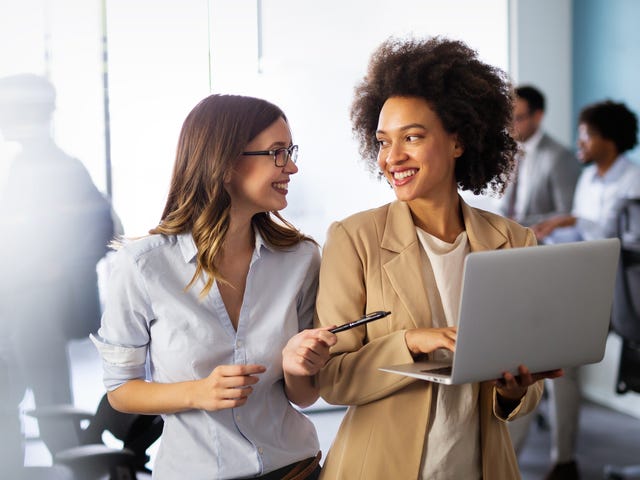 Zwei Frauen stehen mit einem Laptop zusammen und tauschen sich über ihren Sprachkurs aus.