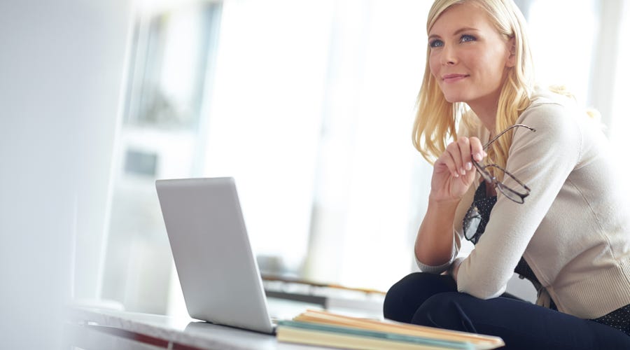 Eine Frau sitzt vor einem Laptop und denkt nach.