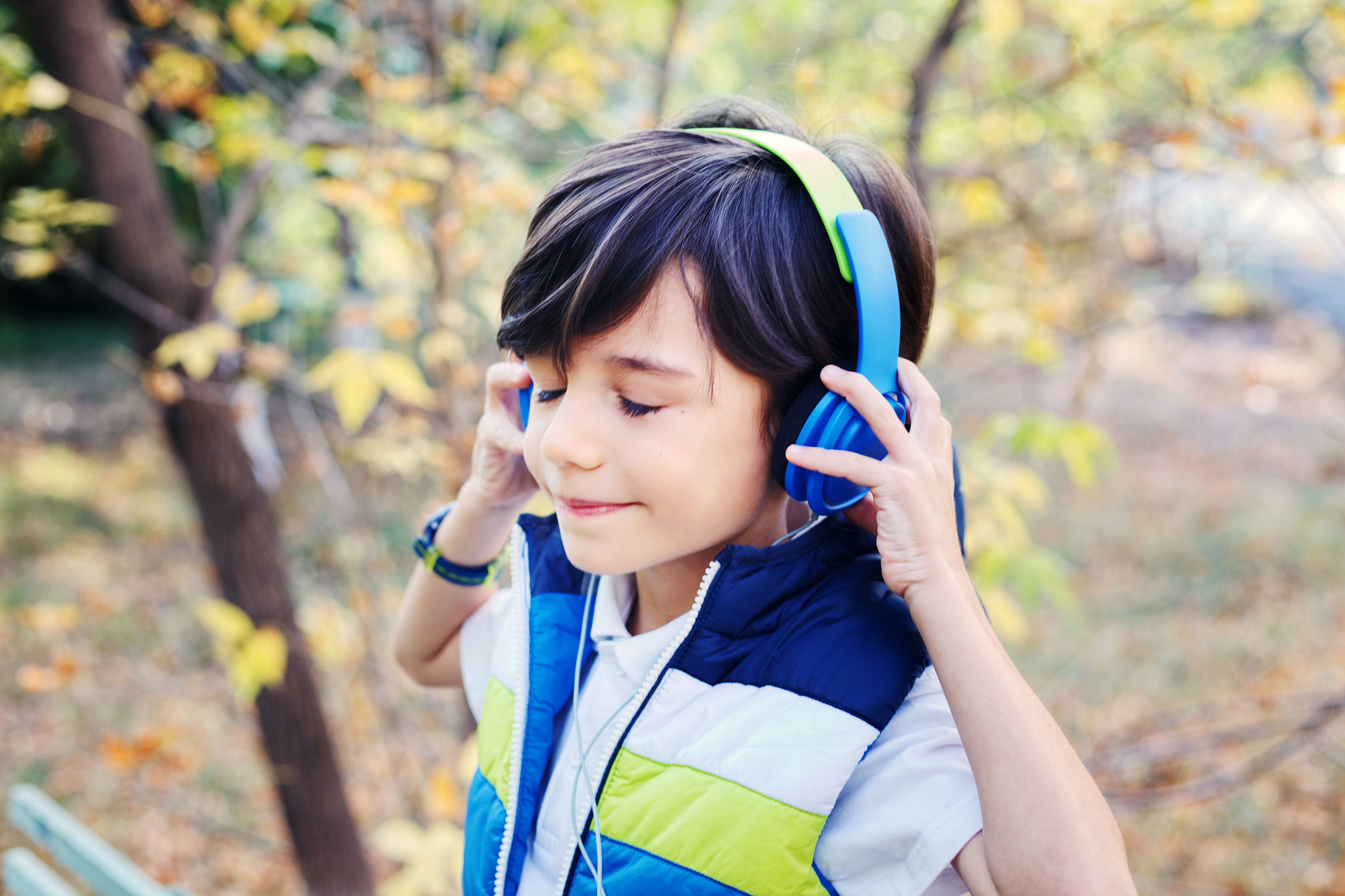 Ein Junge mit Kopfhörern steht in der Natur und hört Musik.