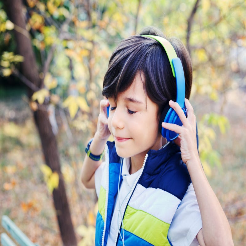 Ein Junge mit Kopfhörern steht in der Natur und hört Musik.