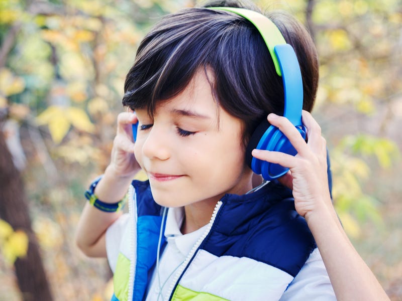 Ein Junge mit Kopfhörern steht in der Natur und hört Musik.