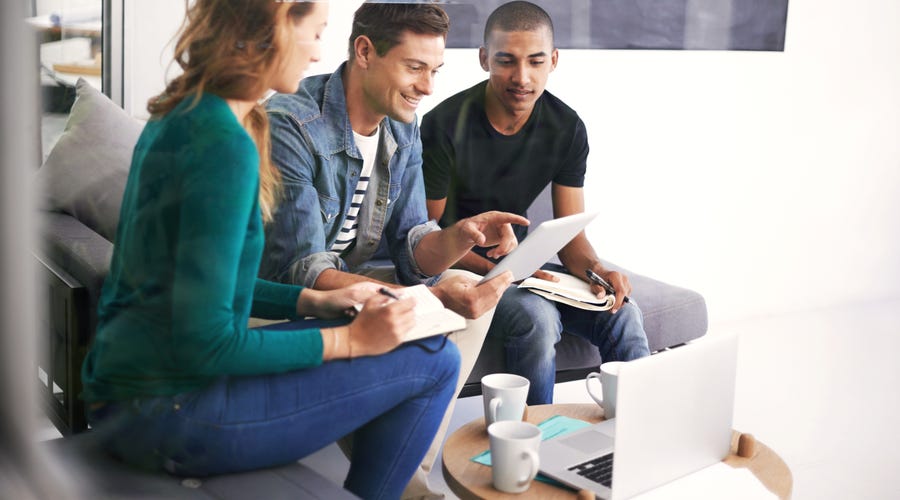 Drei Personen sitzen auf einem Sofa und schauen gemeinsam auf ein Blatt Papier.