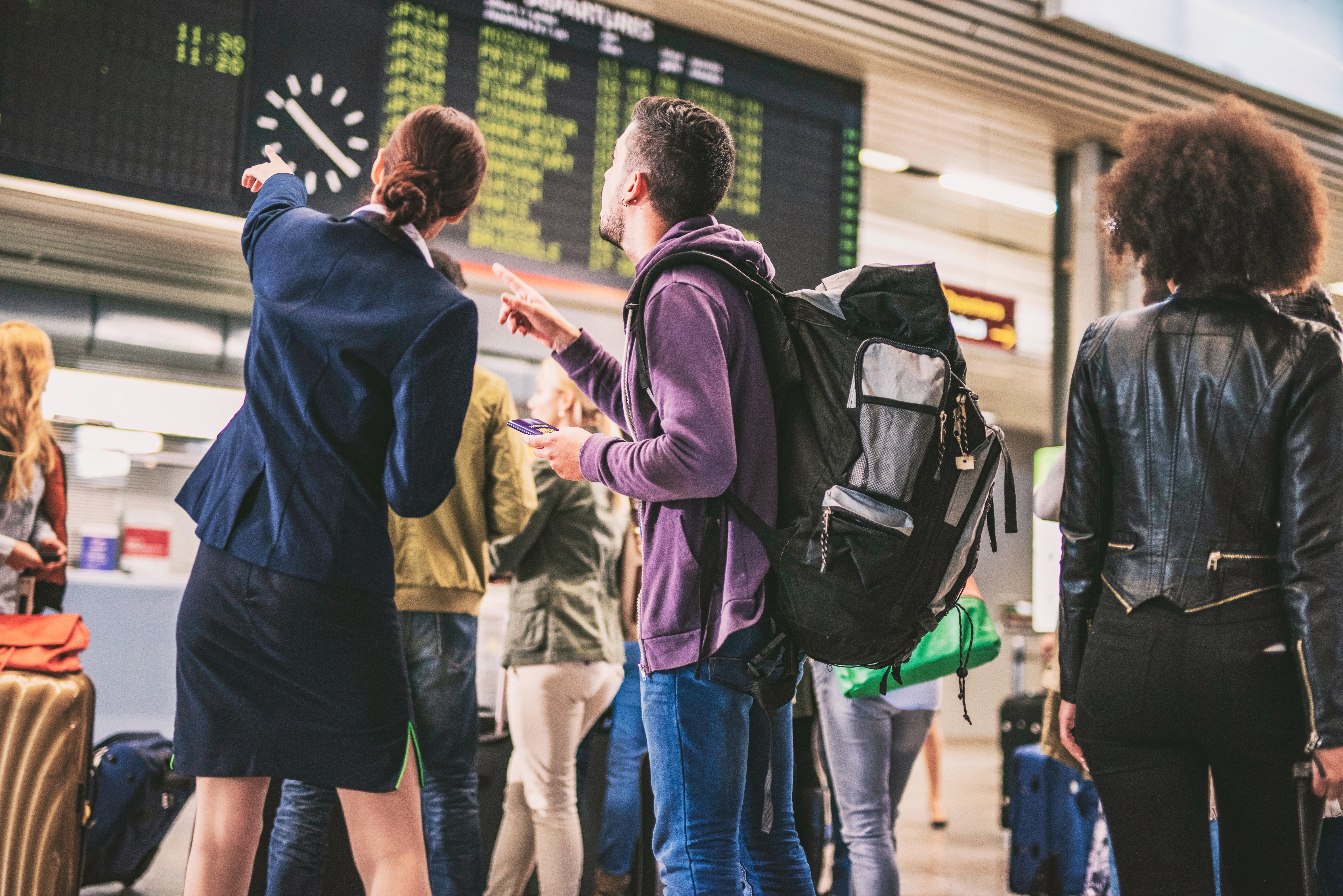 Mehrere Personen stehen am Flughafen zusammen und schauen auf die Anzeigetafel.