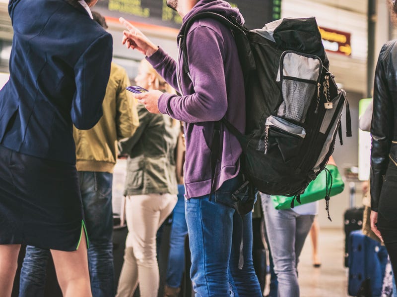 Mehrere Personen stehen am Flughafen zusammen und schauen auf die Anzeigetafel.