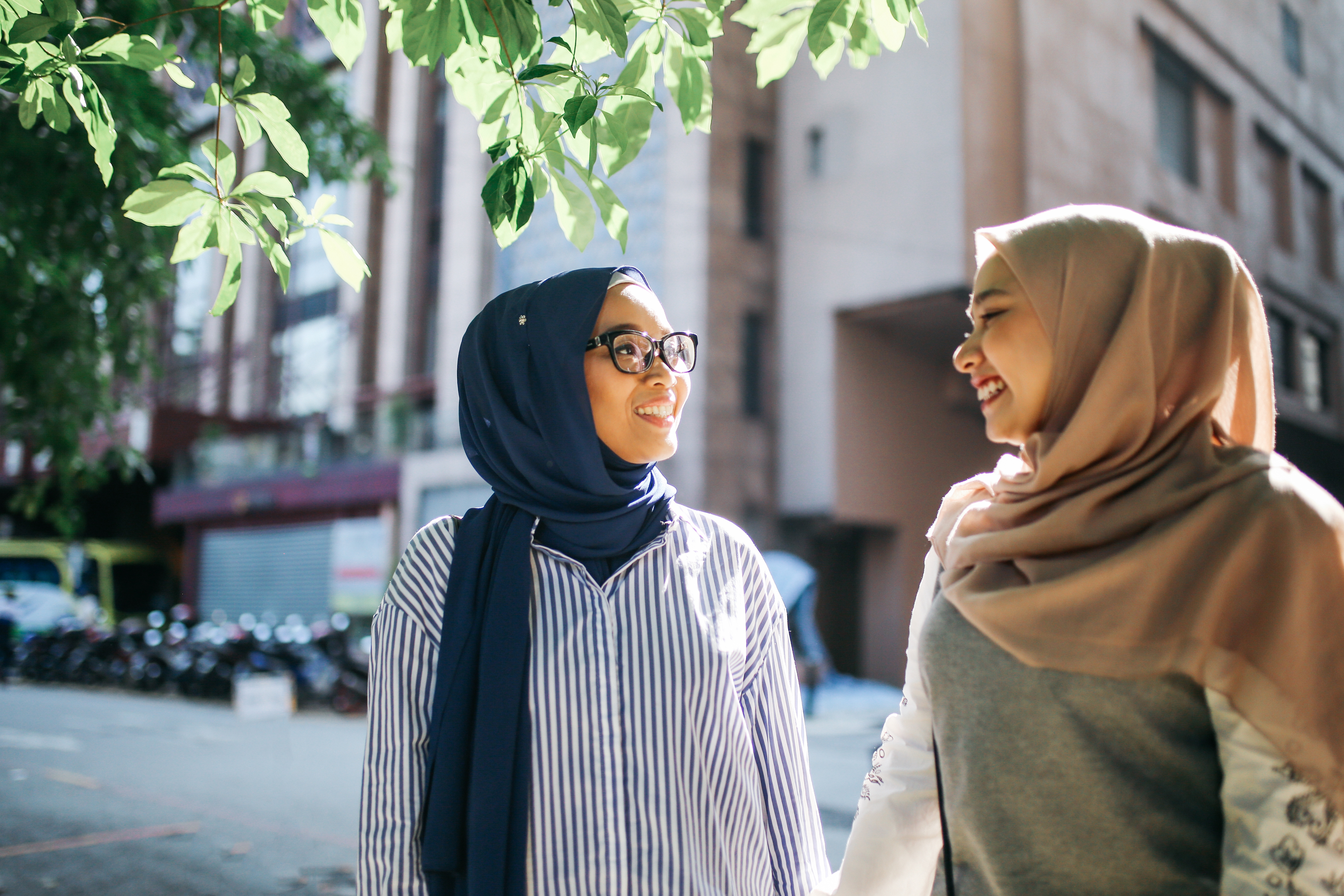 Zwei Frauen stehen unter einem Baum in der Sonne und unterhalten sich.