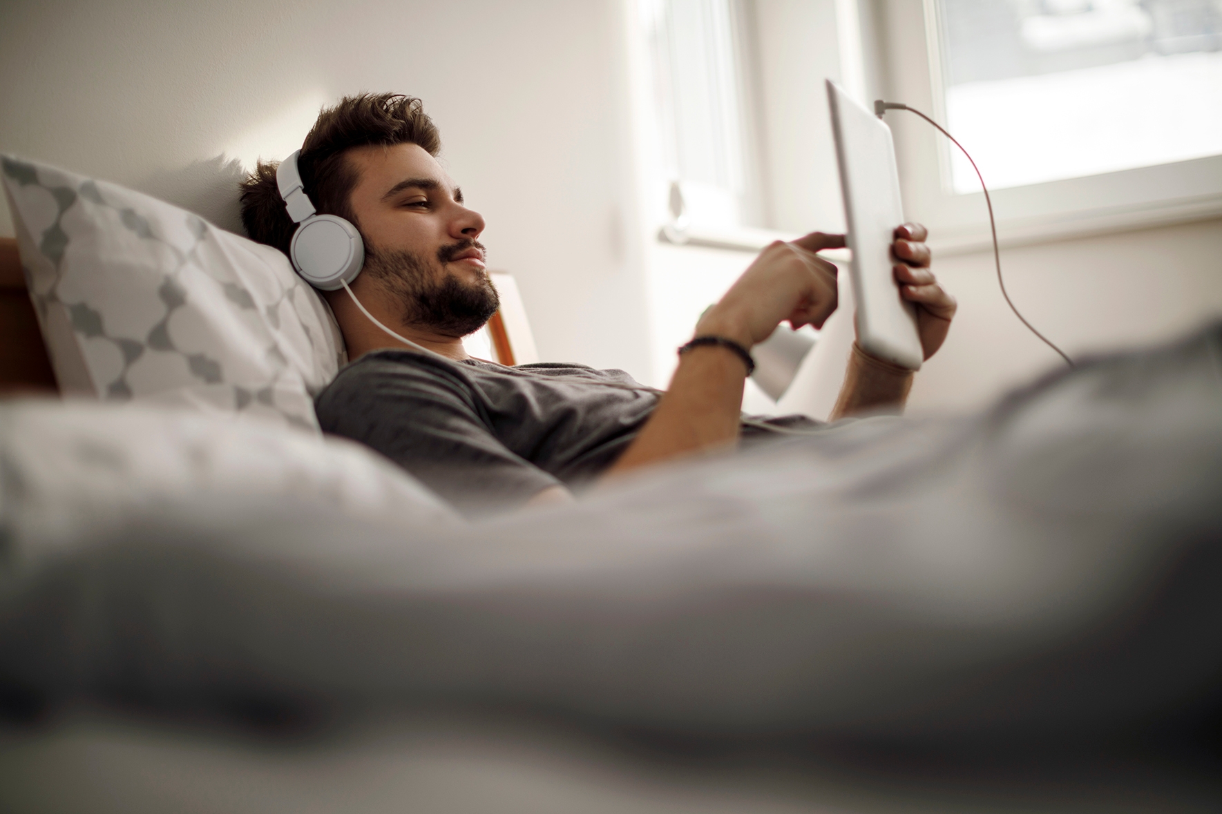 Ein Mann liegt auf dem Bett, mit Tablet und Kopfhörern.