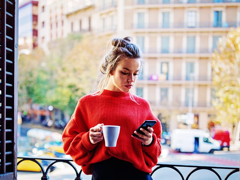 Frau trinkt Kaffee und überprüft Smartphone auf Neuigkeiten.
