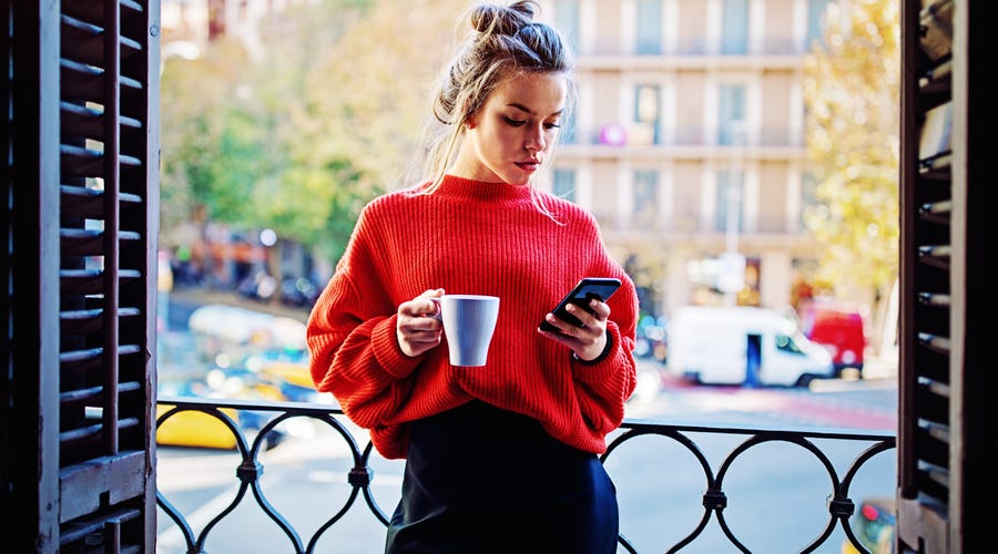 Frau trinkt Kaffee und überprüft Smartphone auf Neuigkeiten.