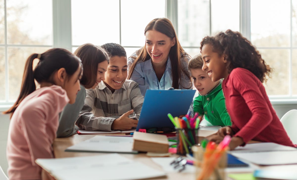 Mehrere Schüler sitzen mit ihrer Trainerin zusammen und unterhalten sich über Aufgaben aus dem Sprachkurs.