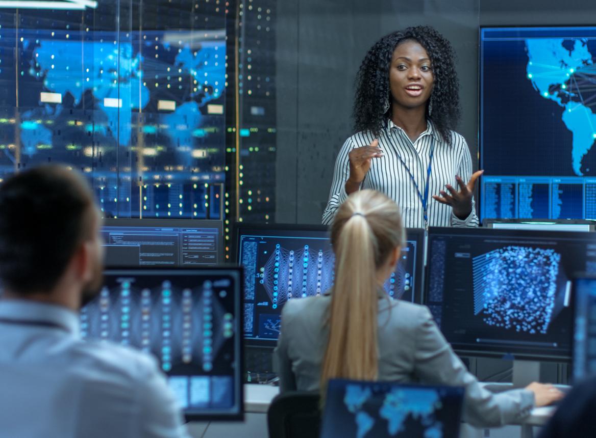 Woman Talking to People at Computers in Front of Servers