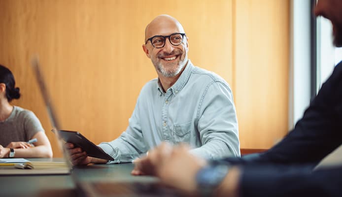 A Man Holding a Tablet and Smiling at a Coworker