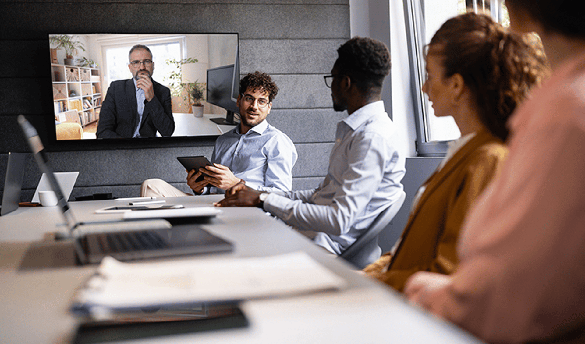 Grid Image & Insights Card: Man on TV Screen Talking to People at Conference Table: 758x446